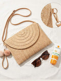 Flat lay front view of beige raffia envelope bag with foldover flap and tan strap