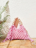 Pink crochet beach bag on tile floor with fern prop hollow knit and fringe sides