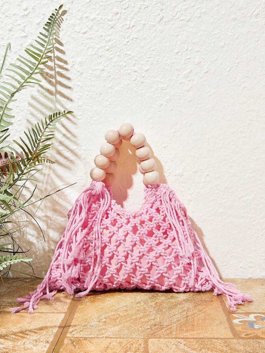 Pink crochet beach bag on tile floor with fern prop hollow knit and fringe sides