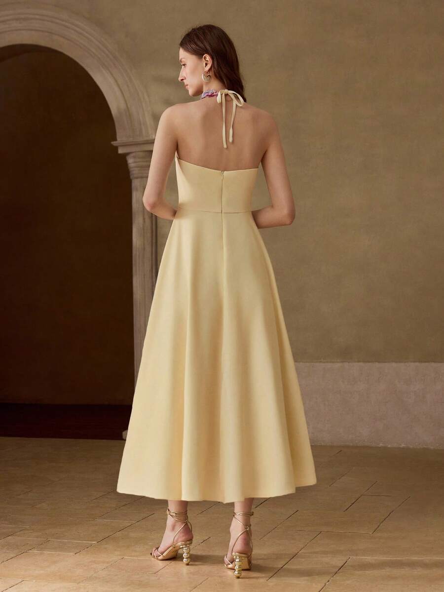 Back view of pale yellow halter midi dress with open back, neck bow, and concealed zipper