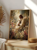 A framed vertical art print leaning against a wall on a wooden console table. The print depicts a serene, painterly scene of Jesus embracing a white sheep in a field of wildflowers.