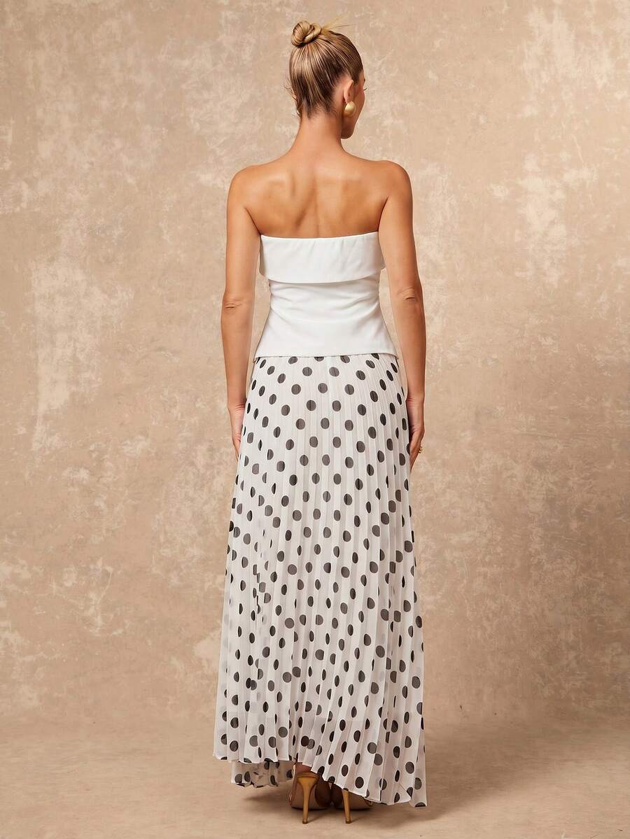 Studio front view of white strapless top with white black polka dot pleated maxi skirt model holding skirt