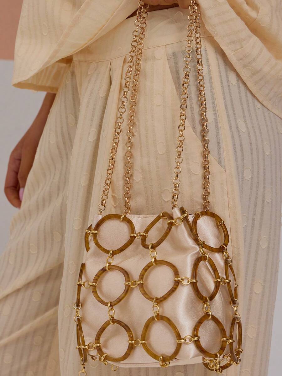 Cream drawstring bucket shoulder bag with tortoiseshell ring cage and gold chain strap