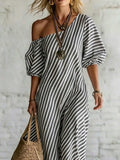 Front crop of grey striped one shoulder dress with voluminous sleeves and straw bag
