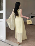 Back view of pale yellow asymmetrical draped chiffon maxi dress showing visible color, trim, and silhouette