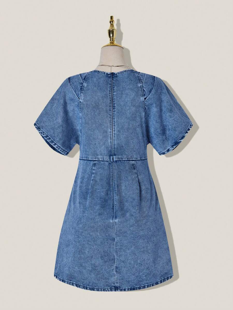 Front view of medium-wash denim mini dress with deep V neck and pleated high-waist bodice