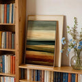Close shelf view of small framed abstract landscape print with books and flowers