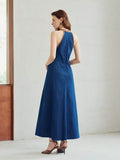 Rear three-quarter view of deep blue sleeveless A-line denim maxi dress in an indoor setting