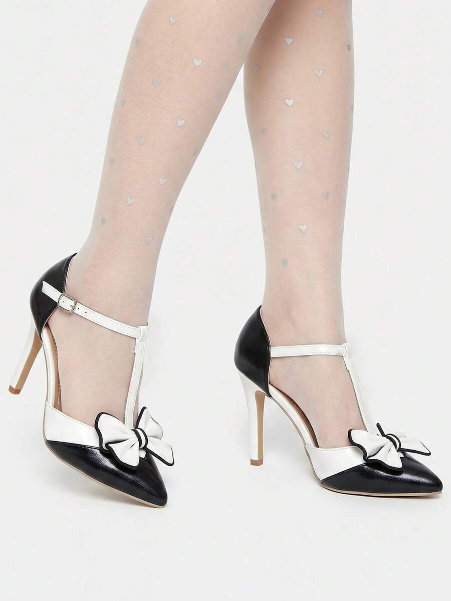 Black and white pointed toe bow pump worn with ankle strap and stiletto heel