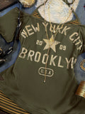 Close-up of olive New York graphic top with distressed Brooklyn lettering and striped insert
