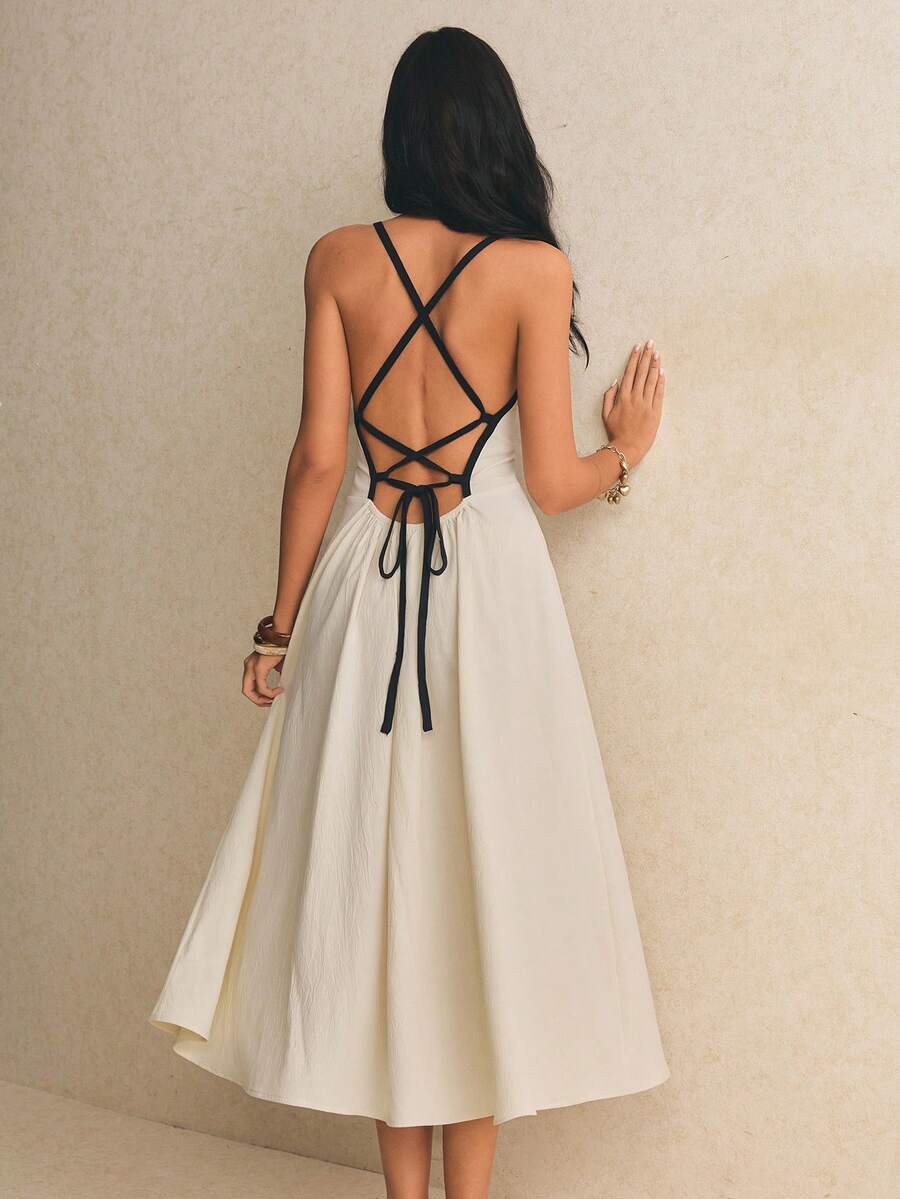 Back full-length view of the apricot midi dress showing an open back, crossed black straps, tie closure, and flowing skirt