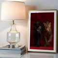 Gold framed leopard panther wall art on stacked books beside table lamp