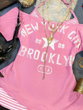 Close-up of pink New York graphic top with distressed Brooklyn lettering and striped insert
