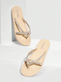 Three-quarter product view of beige rhinestone flip flops on white props