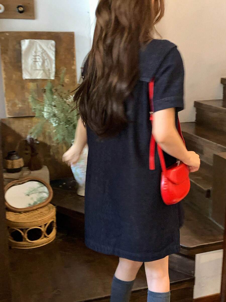 Three-quarter front view of dark-indigo sailor-collar denim mini dress with chest bow and short sleeves