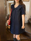 Three-quarter front lifestyle view of dark-indigo sailor-collar denim mini dress with red crossbody bag