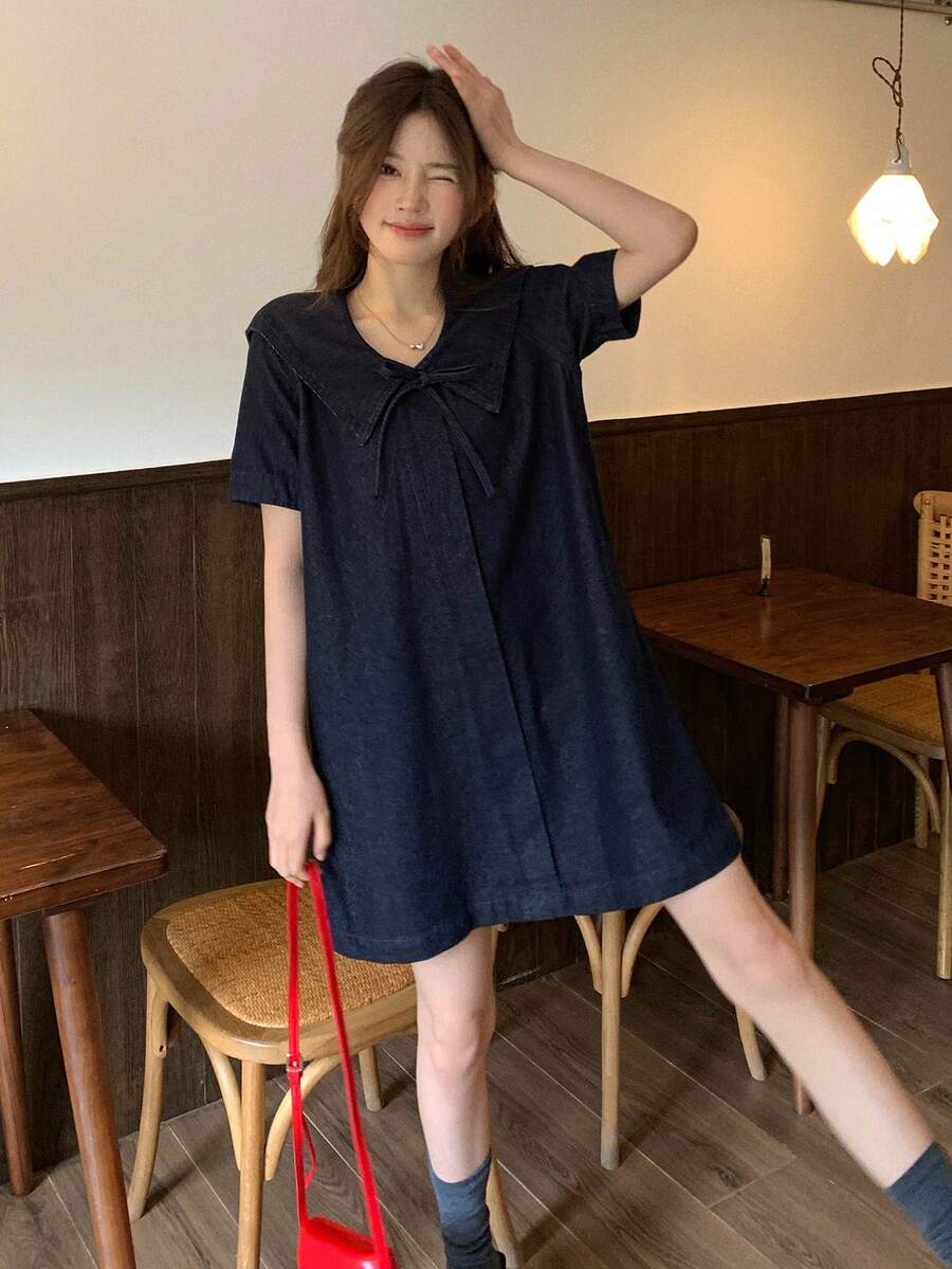 Full front lifestyle view of dark-indigo short-sleeve denim smock dress with flared mini hem
