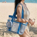 Beach lifestyle view of white mesh tote bag with blue trim and bottle side pocket