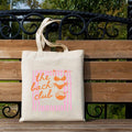 Outdoor bench view of beige canvas tote bag with pink Bach Club swimwear print