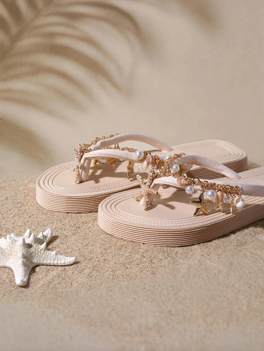 Front three-quarter view of blush beige platform flip flops with shell and starfish charms in a sandy beach setting