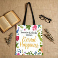 Flat lay front view of white floral Eternal Happiness convention tote bag with books