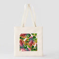 Front view of cream canvas tote bag with colorful tropical leaf square print