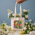 Lifestyle hand-held view of tropical leaf canvas tote bag with long shoulder straps