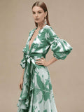 Waist-up view of green botanical maxi dress showing deep V-neck and wide sash bow