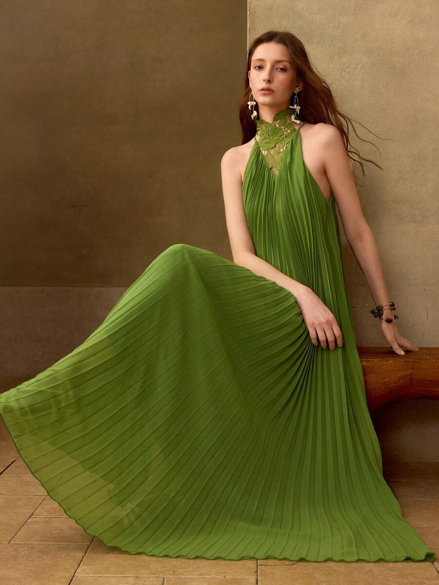 Seated three-quarter view of olive-green lace halter maxi dress with flowing accordion pleats