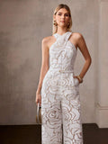 Front three-quarter view of ivory raised-rose jumpsuit styled with gold accessories and mini bag