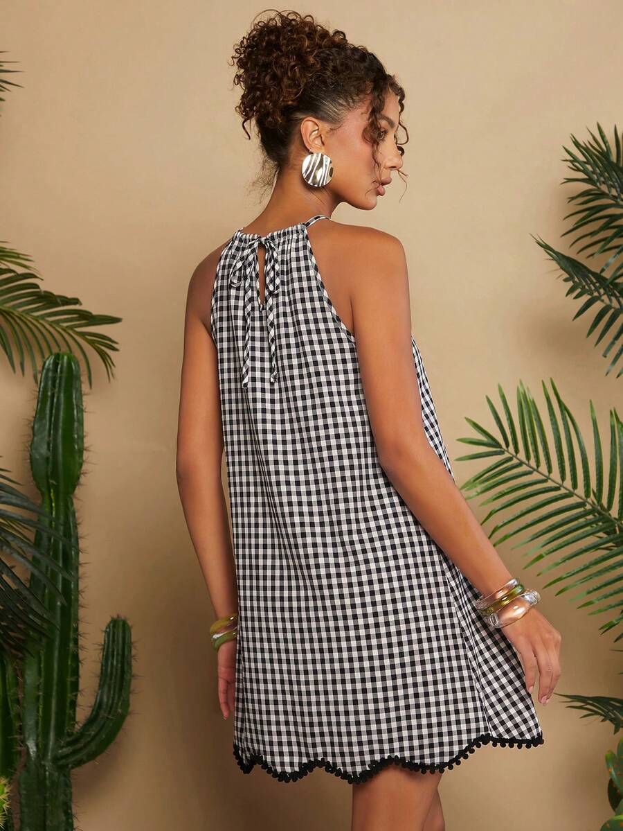 Front view of black and white gingham halter mini dress with pom-pom hem in tropical studio