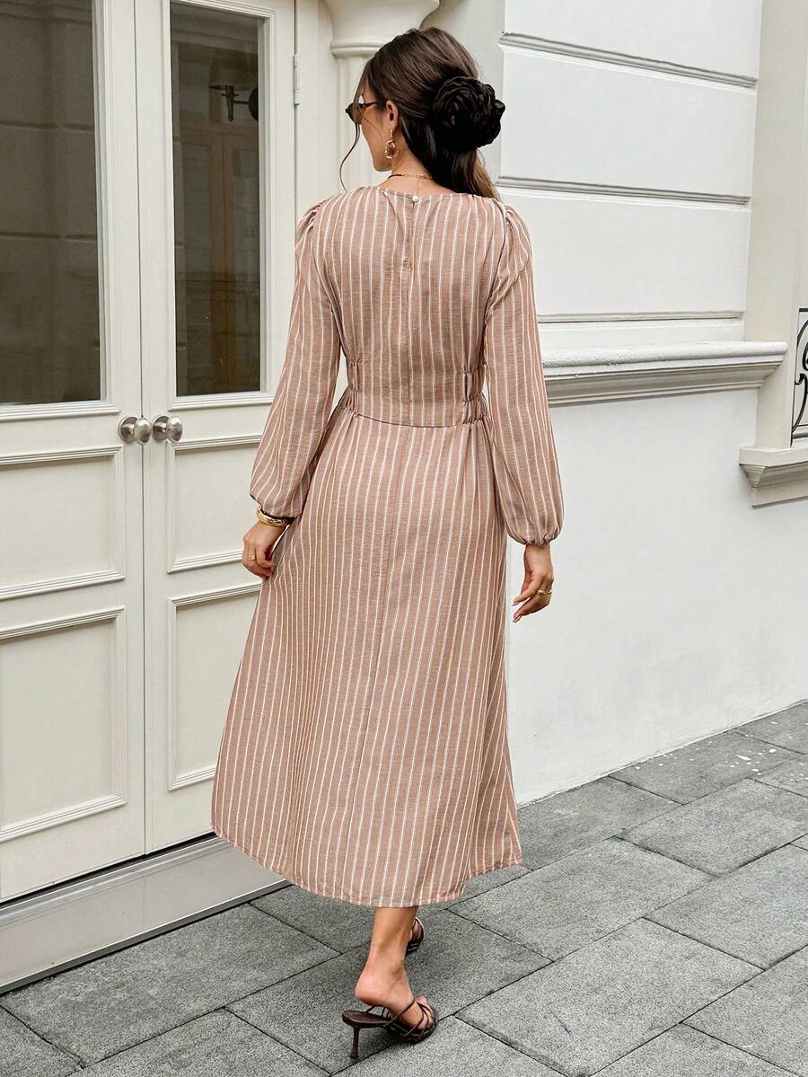Front three-quarter street view of brown striped long-sleeve maxi dress with gathered waist