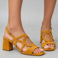 Three-quarter view of mustard yellow strappy square toe block heel sandals on model