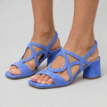 Three-quarter view of periwinkle blue strappy buckle block heel sandals on model