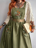 Close-up of floral embroidery and oversized patch pockets on green pinafore dress
