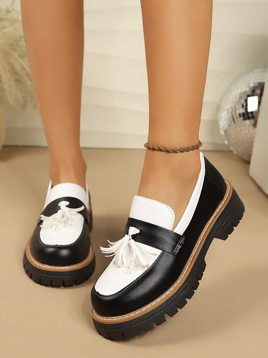 Front-side view of black and white rounded-toe tassel loafers worn indoors