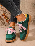 Front-side view of green low-top sneakers with white stripes, pink laces, and round toes