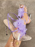 Handheld front view of lavender snakeskin 3D floral cross-strap square-toe stiletto sandals with metallic heel