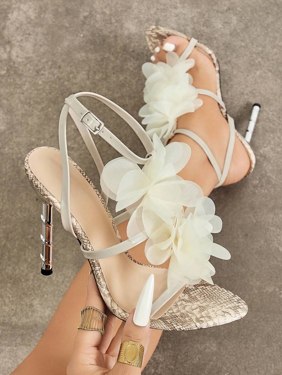 Handheld front view of white and beige 3D floral cross-strap square-toe stiletto sandals with metallic heel