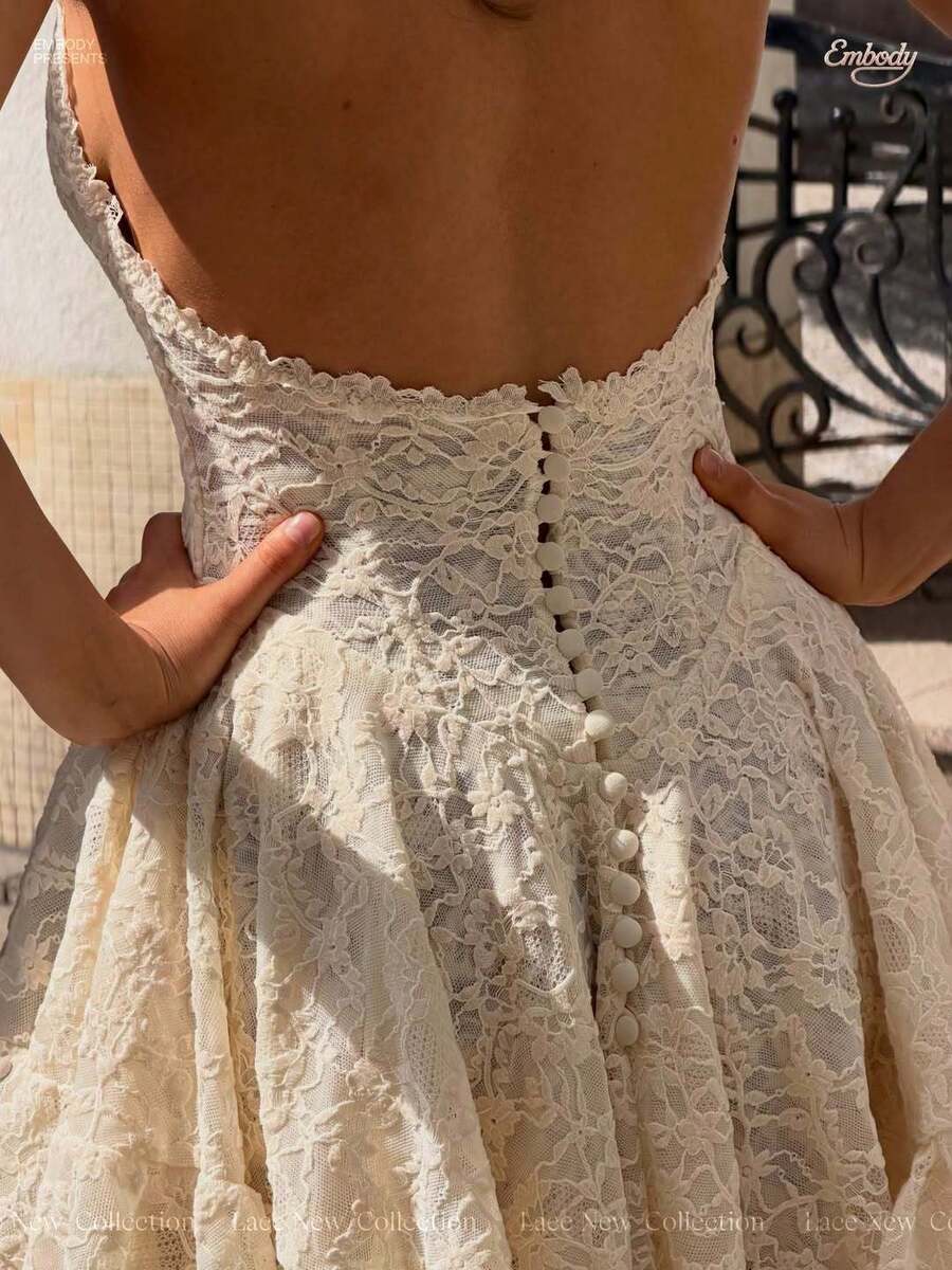 Back close-up of the cream lace mini dress showing an open back, scalloped edge and covered button row