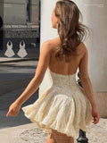 Outdoor rear view of the cream lace halter mini dress showing its low open back and full flared skirt