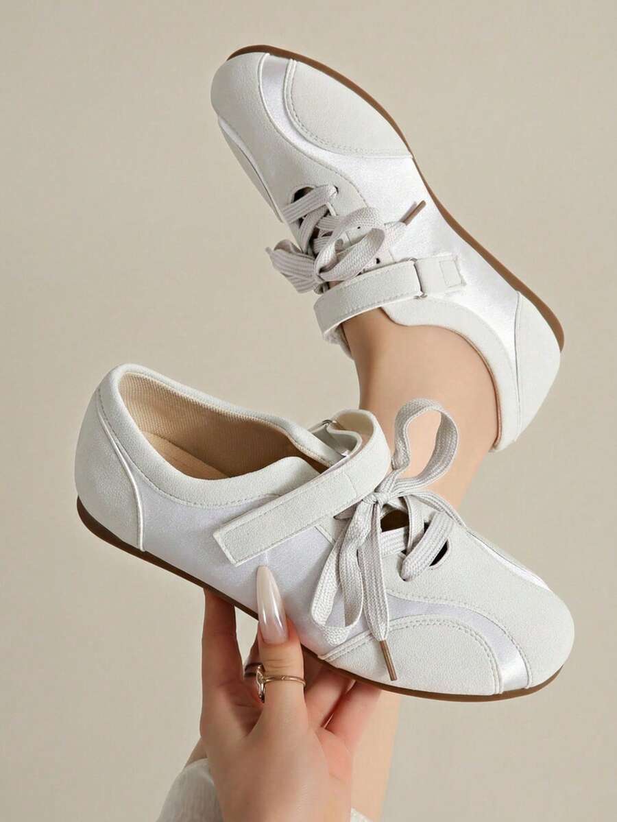 Hand-held front-top view of white lace-up sneakers with hook-and-loop instep straps
