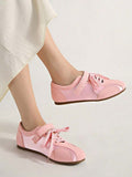 Side view of pale pink rounded-toe strap sneakers worn against a beige studio backdrop