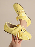 Hand-held front-top view of pale yellow lace-up sneakers with hook-and-loop instep straps