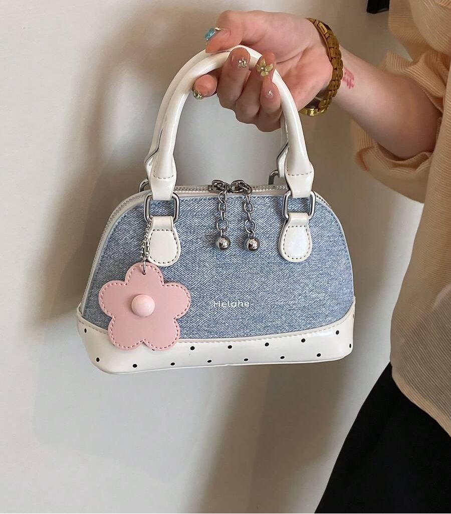 Front view of baby blue dome handbag with cream handles, dotted trim and pink flower charm beside a phone