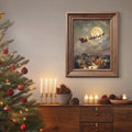 Framed Santa sleigh and snowy village print above a console in a Christmas-decorated room.