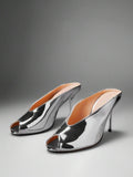 Silver front three-quarter product view of peep-toe stiletto mule sandals with a backless slip-on upper and slim high heel