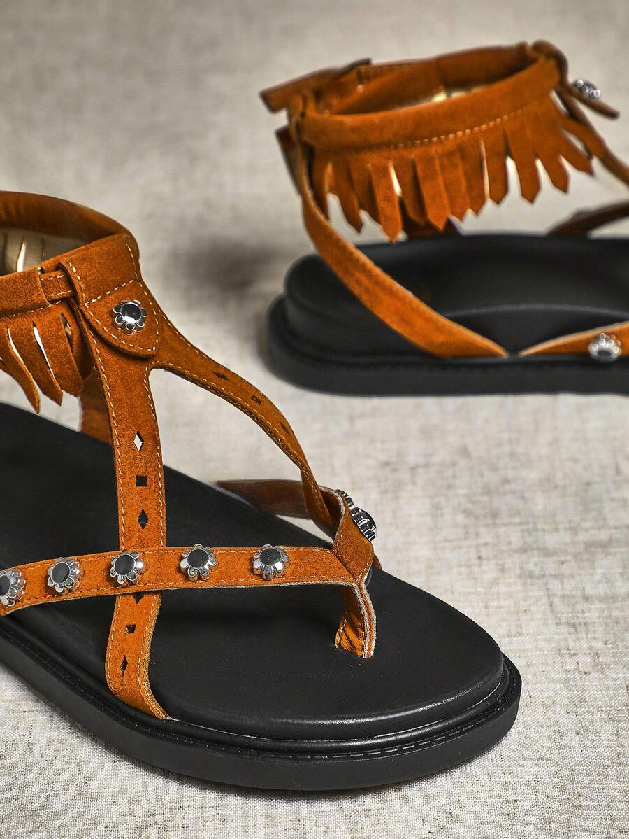 Close-up of chestnut fringe sandal straps with floral metal accents and toe-post detail