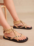 Beige boho fringe ankle-strap flat sandals worn with open-toe cross straps