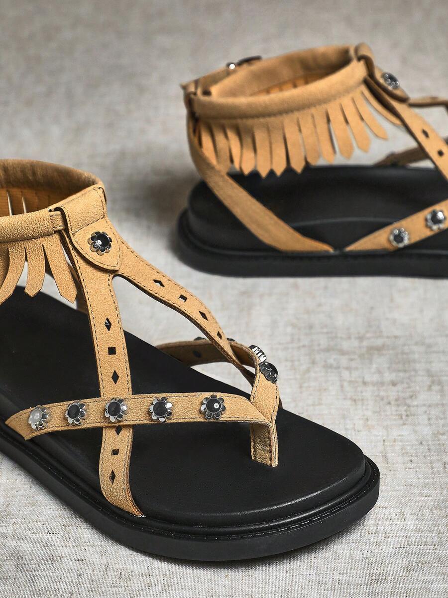 Close-up of beige fringe sandal straps with floral metal accents and toe-post detail